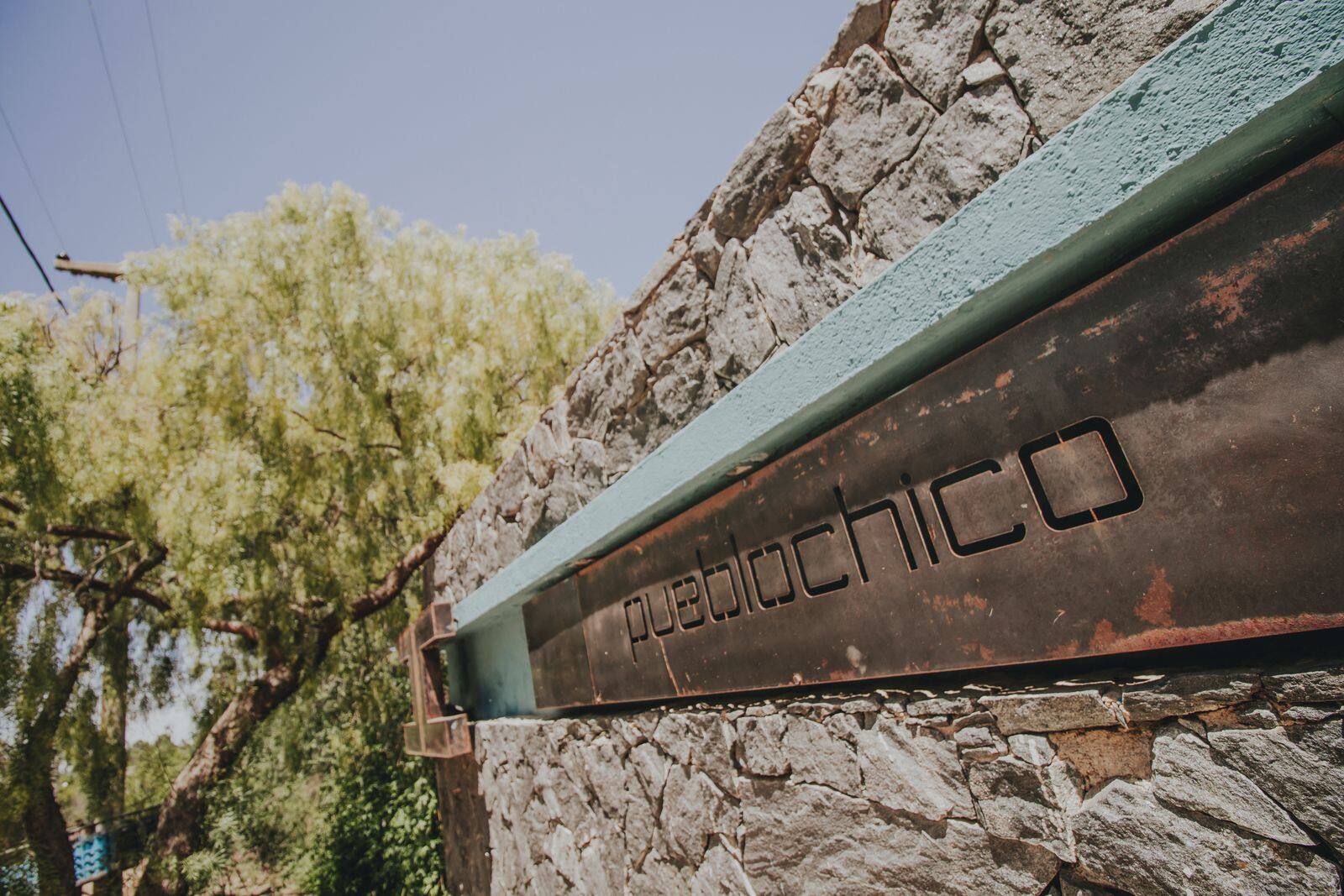 El cartel de Pueblo Chico sobre el muro de piedra de la entrada