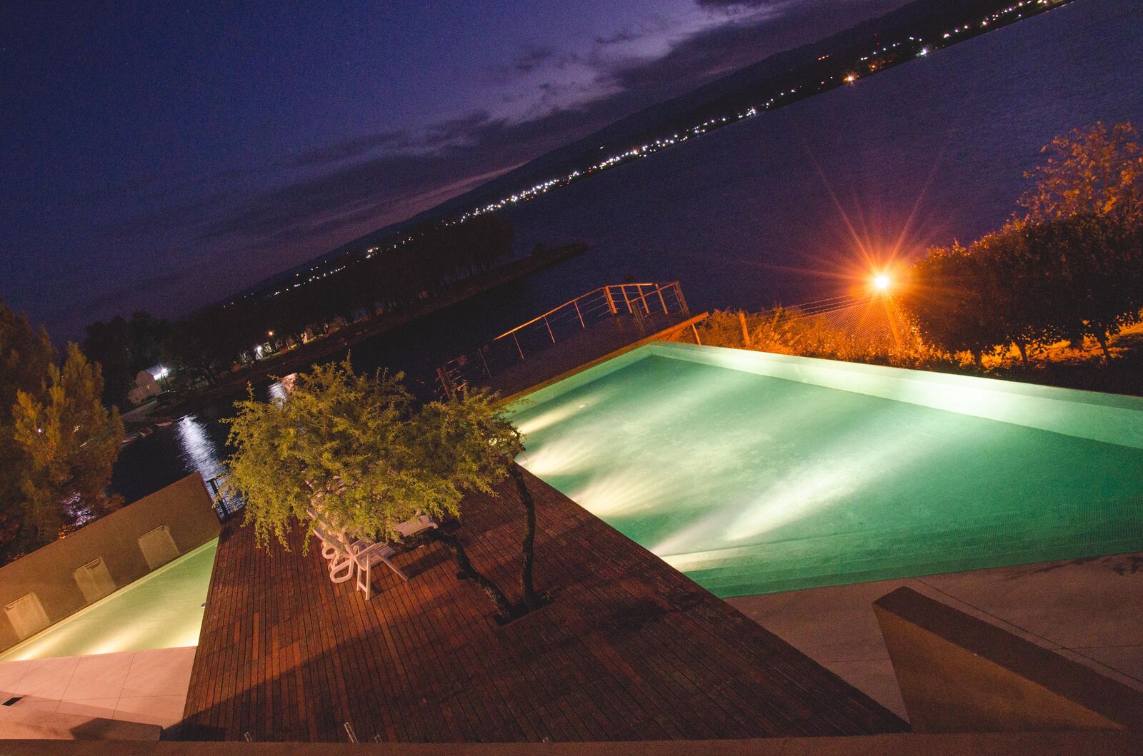 La pileta iluminada de noche, con las luces del pueblo al otro lado del Lago Los Molinos