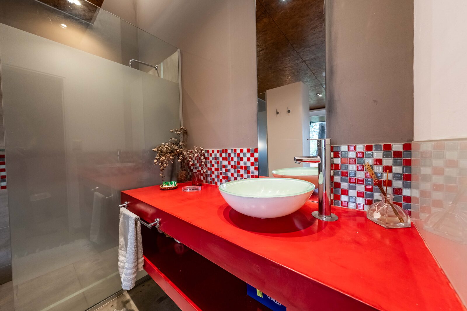 En-suite bathroom of the studio with a white basin on a red counter and mosaic tiles