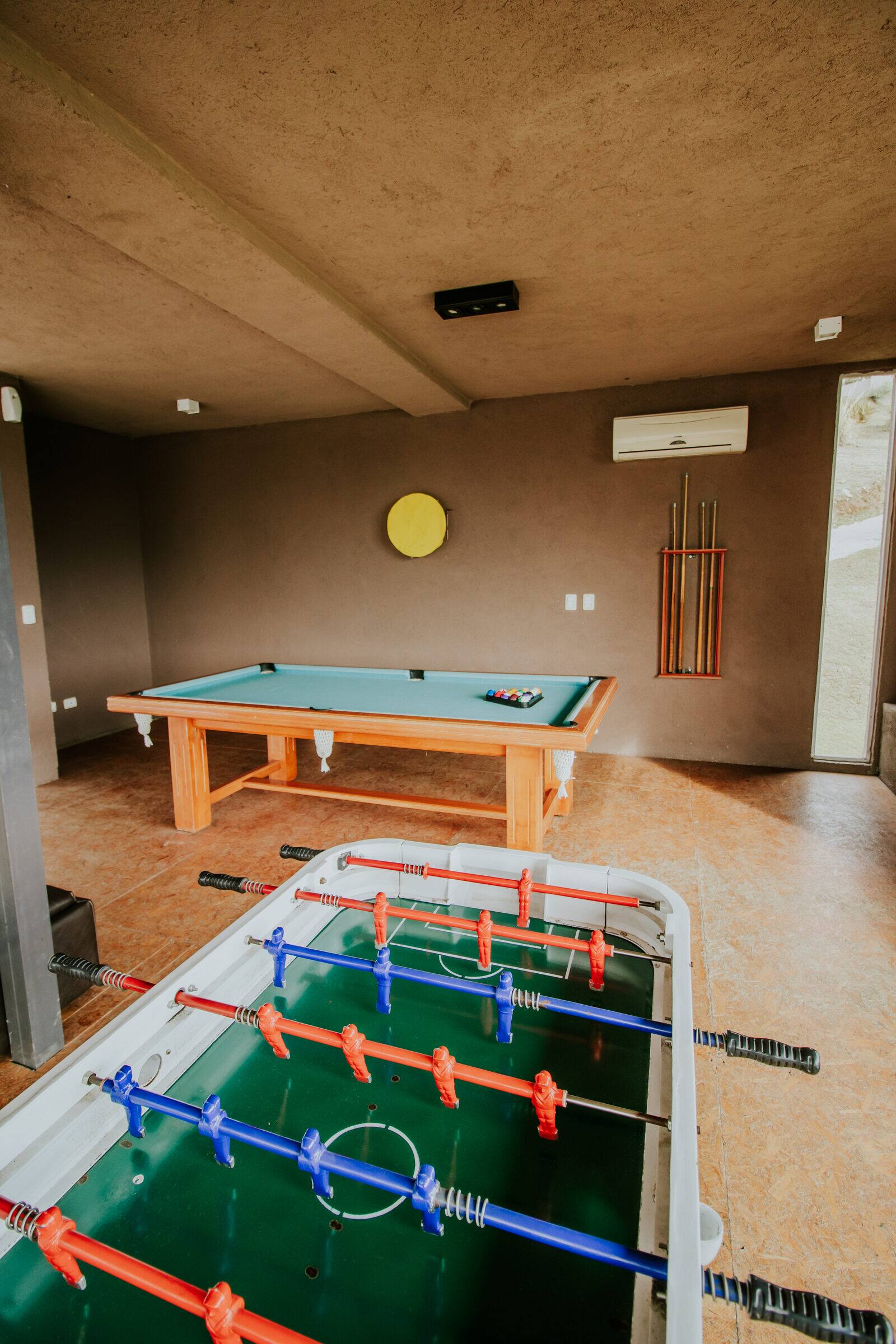 Mesa de billar con los tacos en la pared y metegol en la sala de juegos